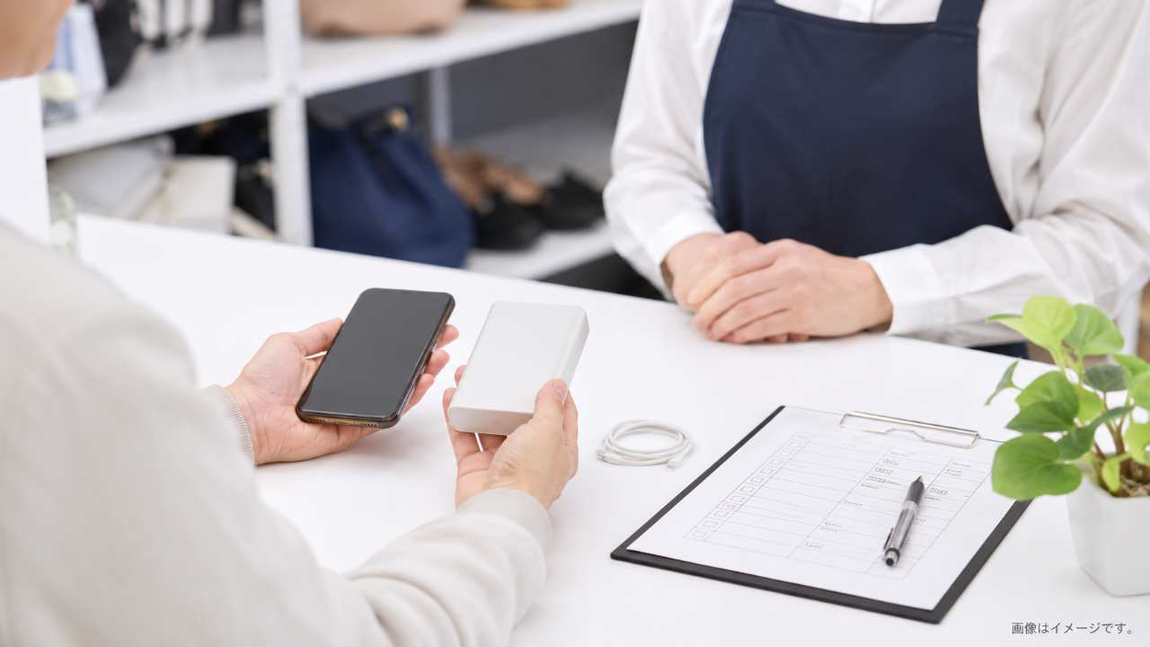 清潔な白いデスクの上にスマートフォン、モバイルバッテリー、USB-Cケーブル、買取査定のチェックシートが自然に並んでいる実写風写真